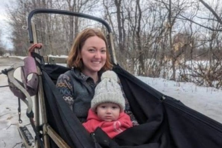Woman and baby in winter clothes on a sled in a snowy landscape.