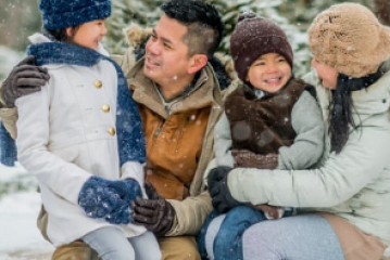 Family sitting in snow wearing winter clothes, smiling at each other.