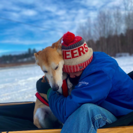 Person in blue jacket hugging a dog on a snowy landscape.
